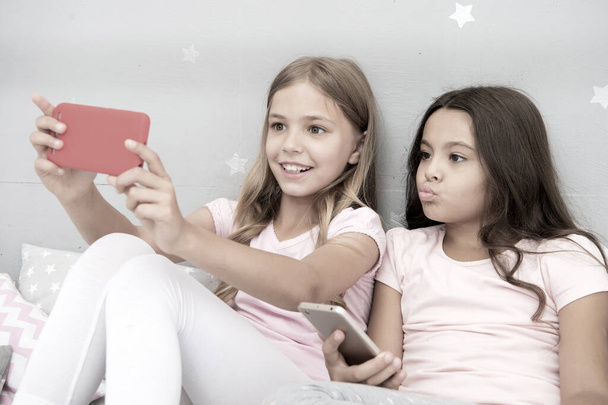 Kids taking selfie in bedroom. Pajamas party concept. Girlish leisure happy childhood. Girls long hair with smartphones use modern technology. Lets take selfie. Send photo your friends social network - Foto, Imagem