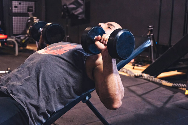 Athlétique jeune homme séance d'entraînement dans la salle de gym avec haltères. - Photo, image