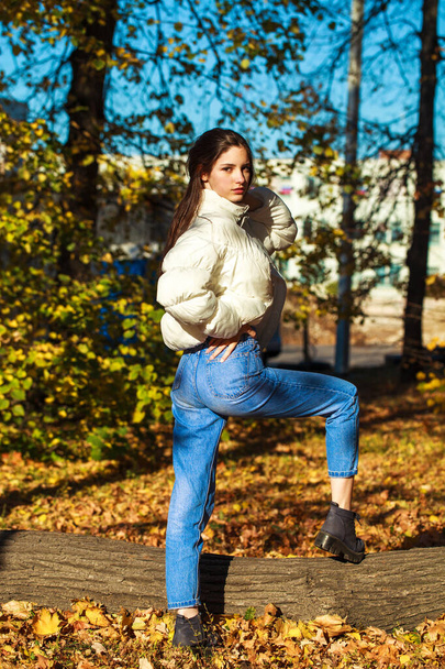 Full body portrait of a young beautiful brunette girl in blue jeans, autumn park outdoor - 写真・画像