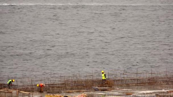 travailleurs de la construction travaillant au bord de la mer journée nuageuse. travailleurs de la construction travaillant avec des barres d'armature - Séquence, vidéo