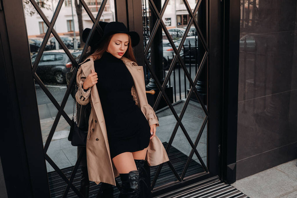 Stylish young woman in a beige coat in a black hat on a city street. Womens street fashion. Autumn clothing.Urban style - Foto, afbeelding