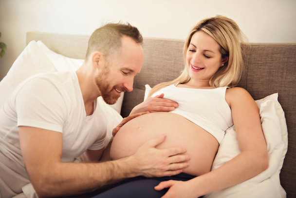 Beautiful pregnant woman and her handsome husband spending time together in bed - Φωτογραφία, εικόνα