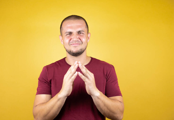 Ruský muž v základním červeném tričku přes žluté izolované pozadí s rukama u sebe a prsty zkříženýma na úsměvu uvolněně a vesele. Úspěch a optimismus - Fotografie, Obrázek