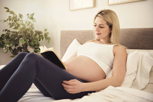 pregnant woman on the bed at home with book - 写真・画像