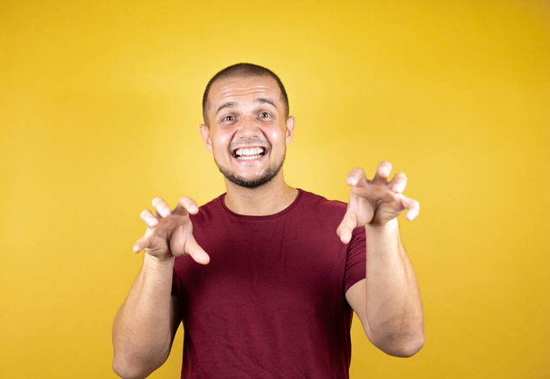Homme russe portant t-shirt rouge de base sur fond jaune insolé souriant drôle faisant griffe geste comme chat, expression agressive et sexy - Photo, image