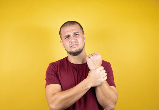 Uomo russo indossa base t-shirt rossa su sfondo giallo insolato Sofferenza dolore alle mani e alle dita, infiammazione dell'artrite - Foto, immagini