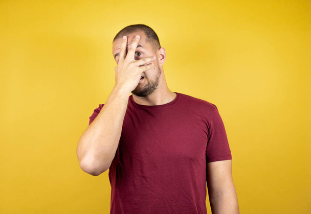 Русский мужчина в обычной красной футболке на желтом инсоляционном фоне с грустным и испуганным выражением лица. Смущенная и негативная концепция. - Фото, изображение
