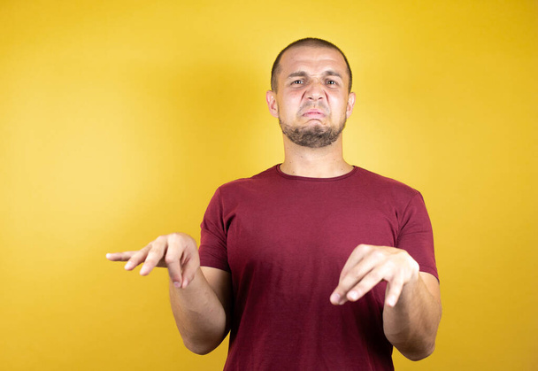 Russischer Mann in einfachem rotem T-Shirt über gelbem isoliertem Hintergrund angewiderte Miene, ungehalten und ängstlich dabei Ekel Gesicht, weil Abneigung Reaktion. Mit erhobenen Händen. Ärgerliches Konzept - Foto, Bild