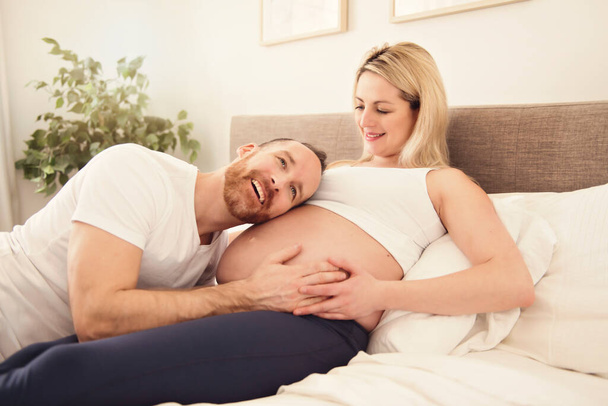 Beautiful pregnant woman and her handsome husband spending time together in bed - Photo, Image