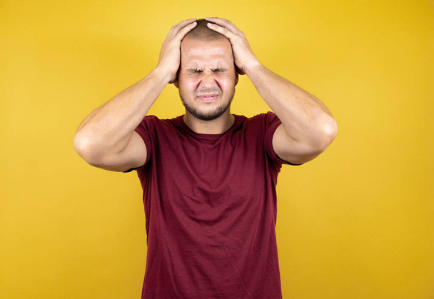 Russische man draagt rode basic t-shirt over gele gesoldeerde achtergrond lijdt aan hoofdpijn wanhopig en gestresst omdat pijn en migraine met haar handen op het hoofd - Foto, afbeelding