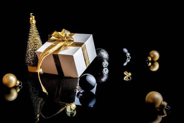 Christmas decoration isolated. White gift with golden bow, gold balls and new year tree in xmas decoration on dark background for greeting card. Christmas, winter, new year concept - Photo, Image