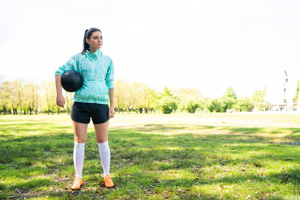 Portrait of young female soccer player standing on field and holding football ball. Sports concept. - Foto, afbeelding