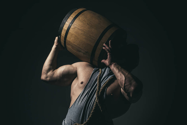 Strong man holds barrel isolated on black. - Foto, Bild