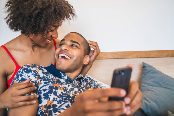 Portrait of happy young latin couple taking a selfie with mobile phone at home. Lifestyle and relationship concept. - Photo, image