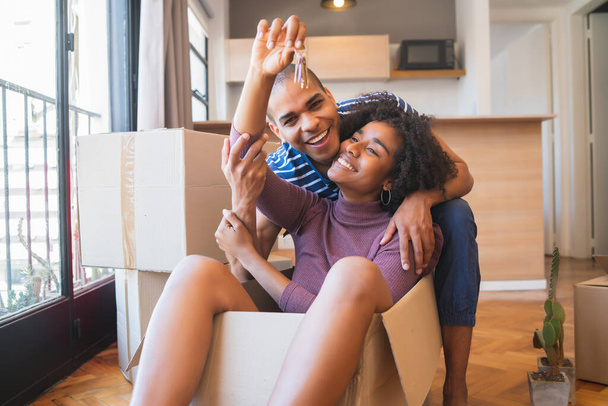 Portrait of happy latin couple having fun with cardboard boxes in new house at moving day. Real estate concept. - Foto, Bild