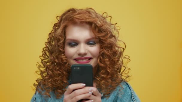 Шокированная девушка читает плохие новости по мобильному телефону на жёлтом фоне - Кадры, видео