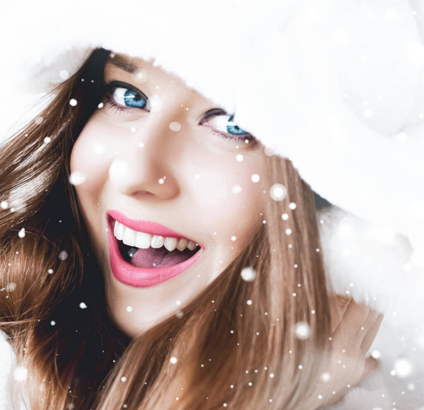 Vánoční a zimní dovolená portrét mladé ženy v bílém kožichu s kapucí, sníh na modrém pozadí, móda a životní styl - Fotografie, Obrázek