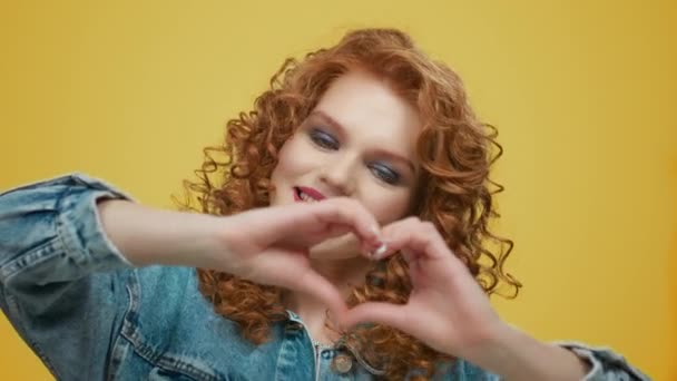 Mujer mostrando señal de corazón. Chica mostrando símbolo de amor sobre fondo amarillo - Imágenes, Vídeo