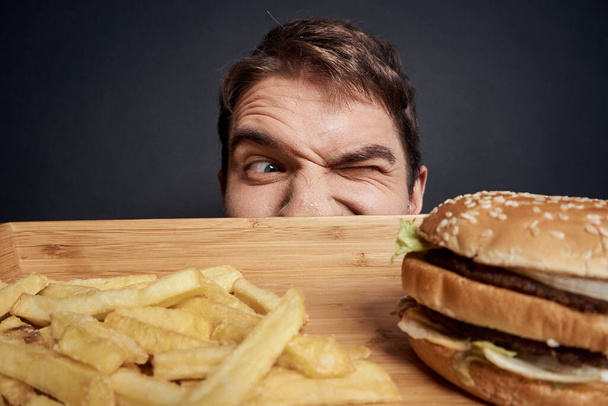 木製パレットのある感情的な男ファーストフードハンバーガーフランス語フライドポテト食生活暗い背景 - 写真・画像