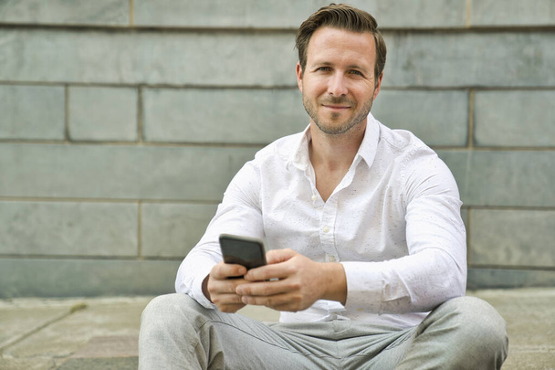 Portrait of an handsome man on the urban background holding phone - Foto, afbeelding