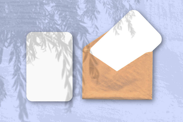 Ein Umschlag mit zwei Blättern strukturierten weißen Papiers auf blauem Hintergrund. Mockup-Overlay mit den Schatten der Pflanze. Natürliches Licht wirft Schatten von einem Weidenzweig. Horizontale Orientierung. - Foto, Bild