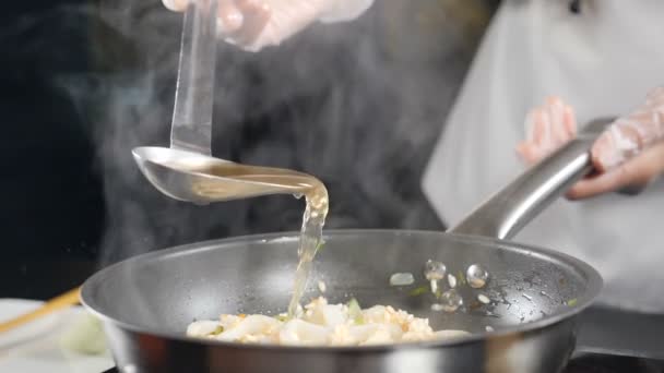 Italiaans visrestaurant. Een close-up van chef-kok die visbouillon van lepel in risotto giet. Langzame beweging. Traditionele Italiaanse keuken. Vol hd - Video