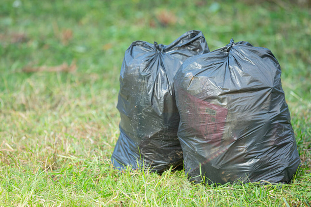 deux sacs poubelles noirs mis sur le sol d'herbe - Photo, image
