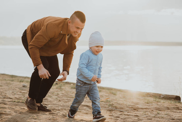 Iloinen isä ja poika leikkivät rannalla rannalla joen rannalla. - Valokuva, kuva