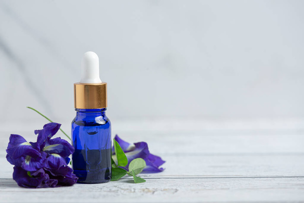 garrafa de soro de óleo de flor de ervilha borboleta colocar no chão de madeira branca - Foto, Imagem