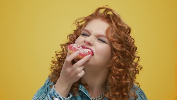 Hongerige vrouw met roze donut in de hand. Meisje eet donut op gele achtergrond - Video