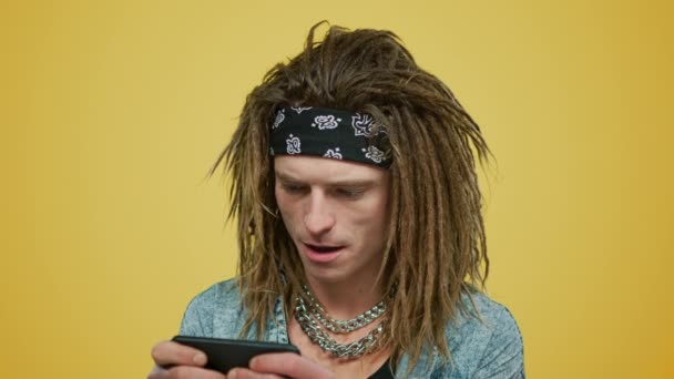 Hombre jugando juego en el teléfono inteligente. Tipo usando el teléfono celular sobre fondo amarillo - Metraje, vídeo