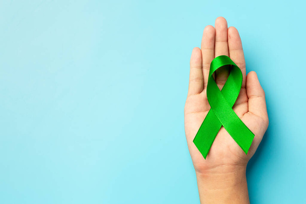 World Mental Health Day; groen lint in de hand van de mens op blauwe achtergrond - Foto, afbeelding