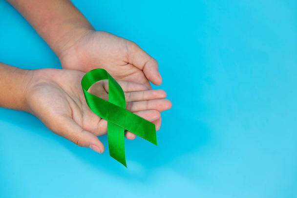 Wereld Geestelijke Gezondheid Dag; groen lint in de handen van de mens op blauwe achtergrond - Foto, afbeelding