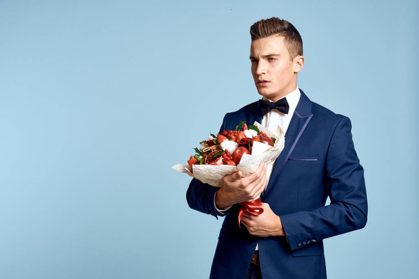 romantischer Mann mit Blumenstrauß und Fliege auf blauem Hintergrund - Foto, Bild