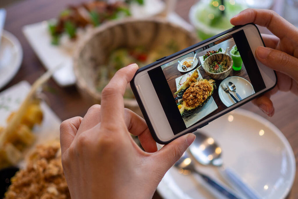 女性は携帯電話を使用して食べ物の写真を撮るか、ソーシャルネットワークアプリケーションでライブビデオを撮影します。夕食の食べ物は食欲をそそるようです。写真とレビューのための写真食品コンセプト - 写真・画像