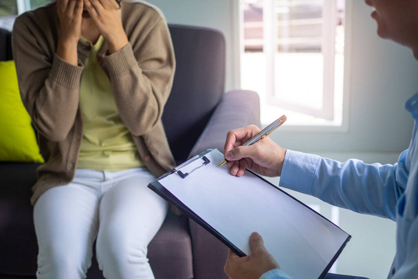 Psychiatrist is advising a young woman with depression. The psychiatrist listens and notes the symptoms to diagnose and find solutions to mental illness. Concept of medical and health services. - Photo, Image