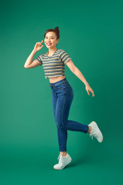 Full-length portrait of a happy young woman dancing on green background - Foto, immagini