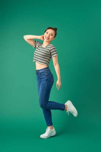Joyful young Asian woman standing on one leg. Full length view of blissful girl dancing on green background. - Photo, Image