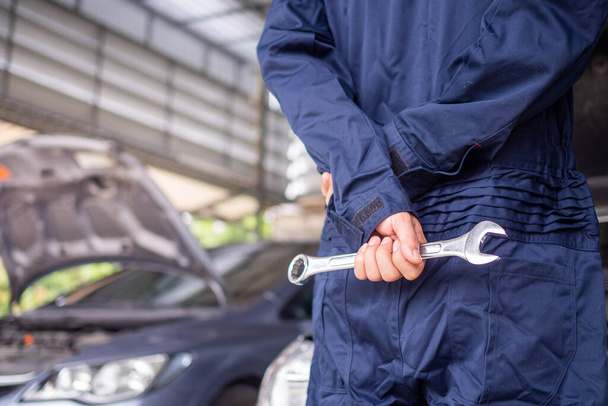 The mechanic in hand with a screwdriver prepared to provide maintenance. The car mechanic standing in the garage has a background image as the car opens up in front of the car preparing for repairs. - Фото, изображение