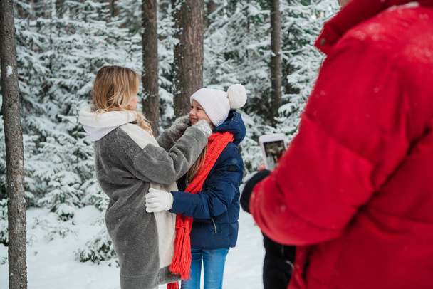 Family photo shoot in the winter snow forest for a beautiful woman and a cute girl on your smartphone - Photo, Image