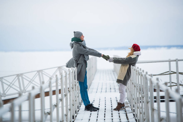冬休みに男と女が一緒に過ごし、雪に覆われた川の桟橋を歩いている - 写真・画像