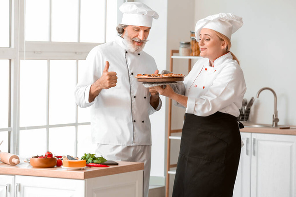 Starší kuchaři s chutnou pizzou v kuchyni - Fotografie, Obrázek