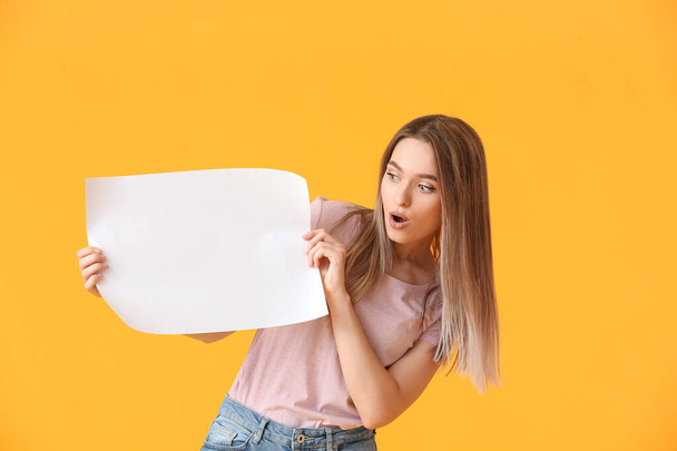 Удивлённая молодая женщина с чистым листом бумаги на цветном фоне - Фото, изображение