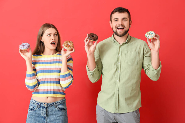 Young couple with sweet donuts on color background - Photo, Image