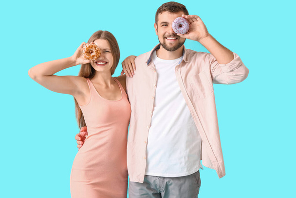 Young couple with sweet donuts on color background - Zdjęcie, obraz