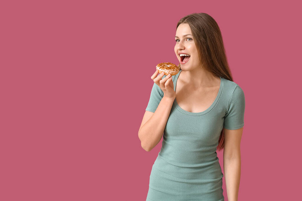 Beautiful young woman with sweet donut on color background - Фото, изображение