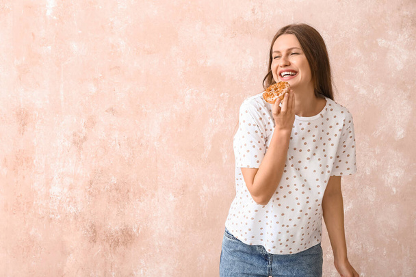 Όμορφη νεαρή γυναίκα με γλυκό ντόνατ στο φόντο χρώμα - Φωτογραφία, εικόνα