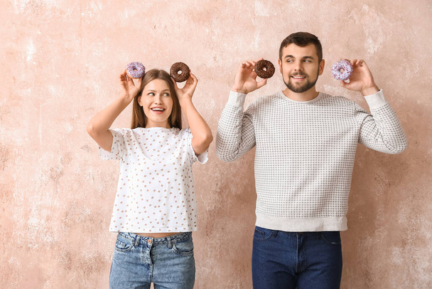 Молодая пара со сладкими пончиками на цветном фоне - Фото, изображение