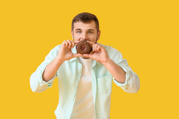 Handsome young man with sweet donut on color background - Photo, Image