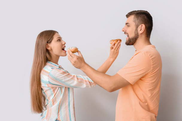 Young couple with sweet donuts on white background - Foto, Imagen